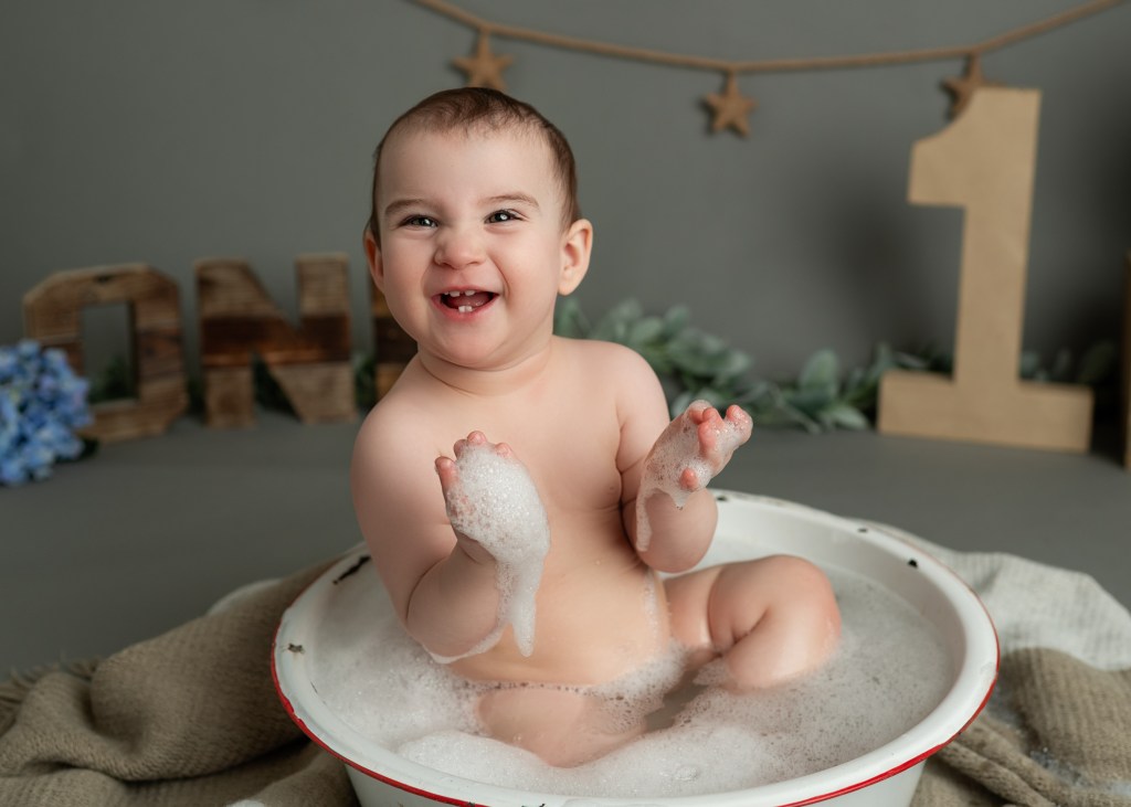 Adorable toddler enjoying a fun-filled cake smash session, covered in colorful frosting with a big smile. A messy, sweet celebration captured in a joyful moment!